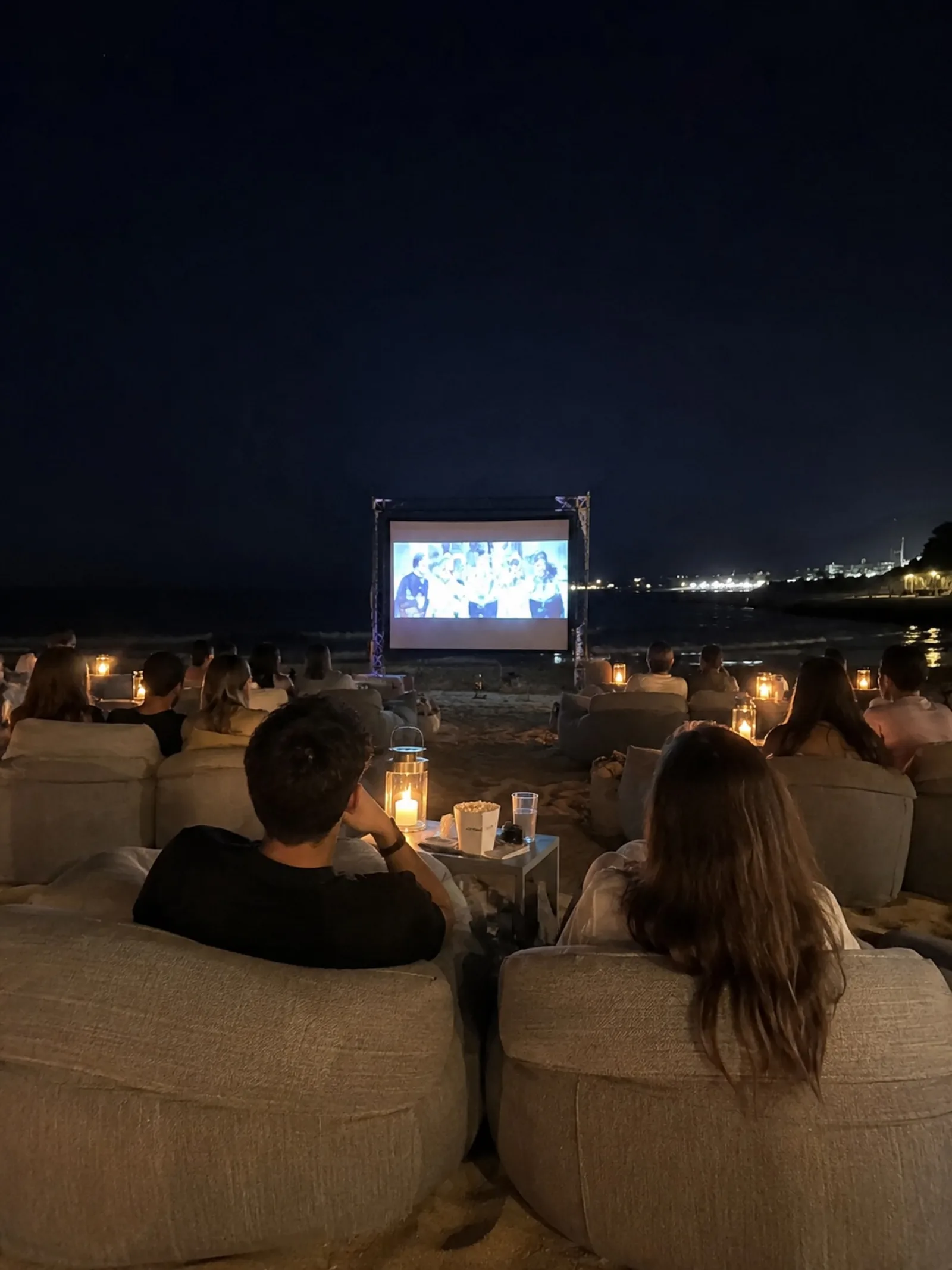 The audience on beanbags after dark, the screen lit and the coast road beyond