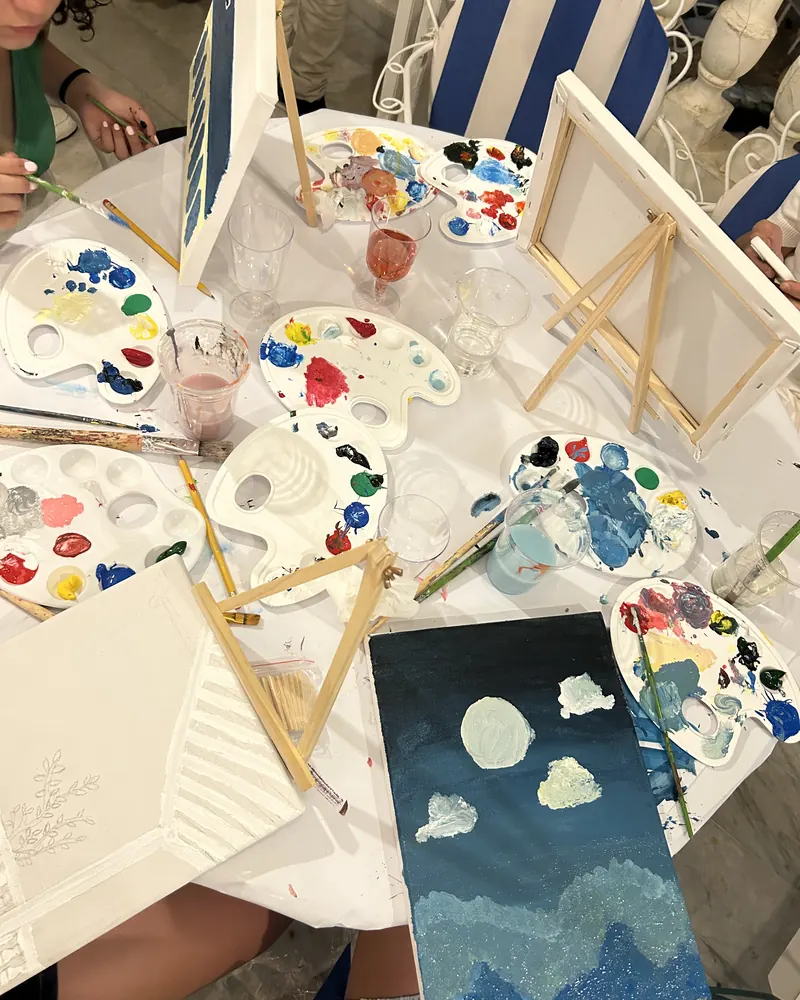 Loaded palettes, brushes and part-finished canvases across a table