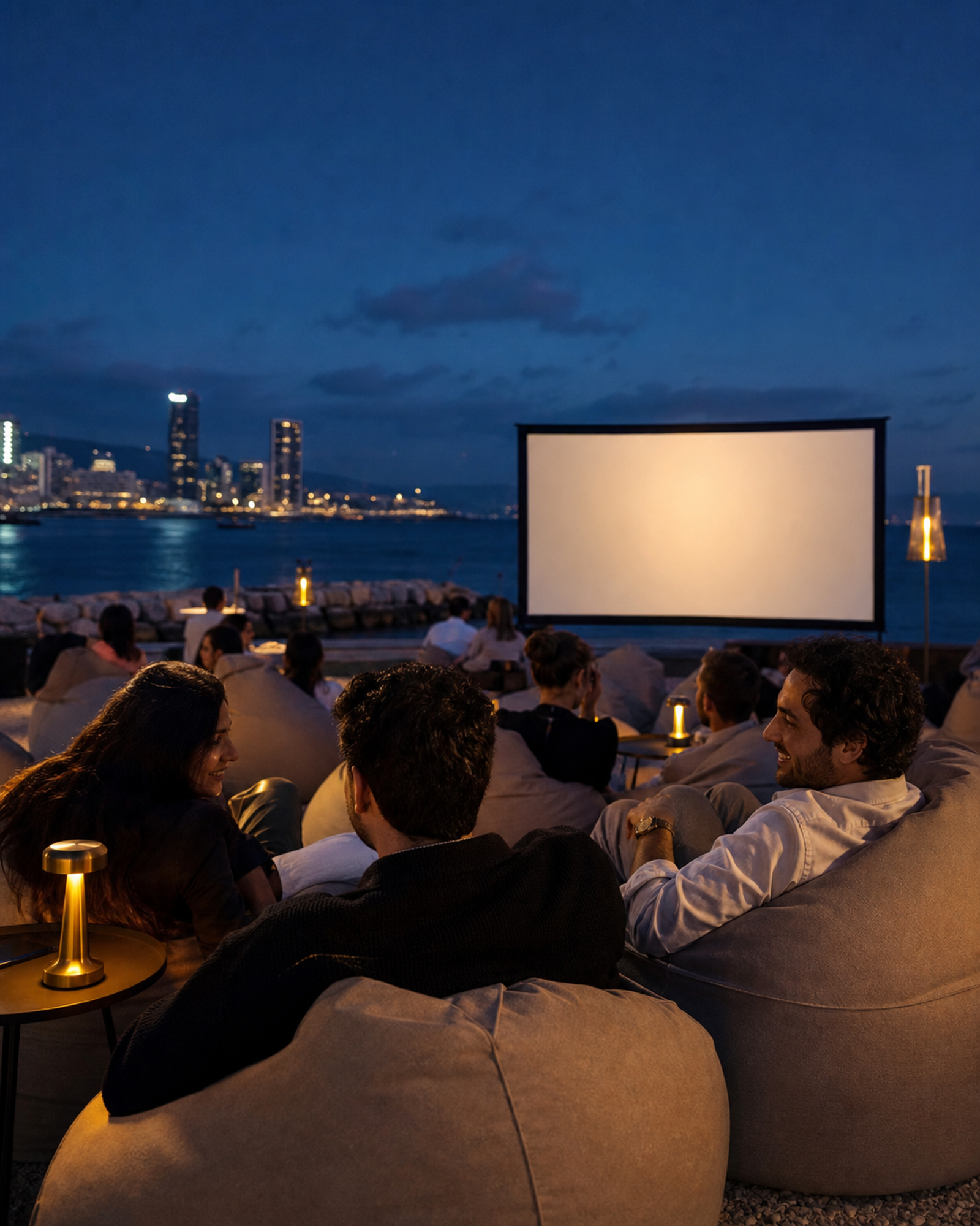 Adult guests enjoying relaxed beanbag seating in front of a waterfront cinema screen.